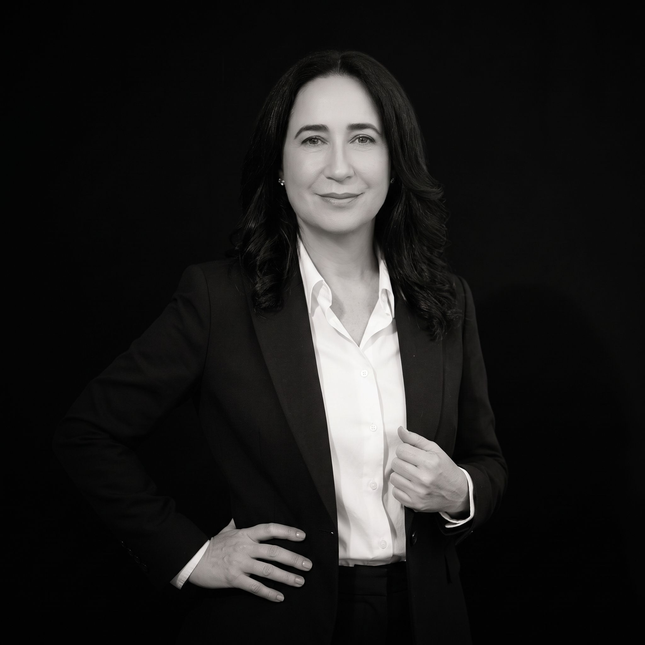 Eva Alfaro G., Mind Coach, de saco negro y camisa blanca, con una mano en la cintura, retrato en blanco y negro.